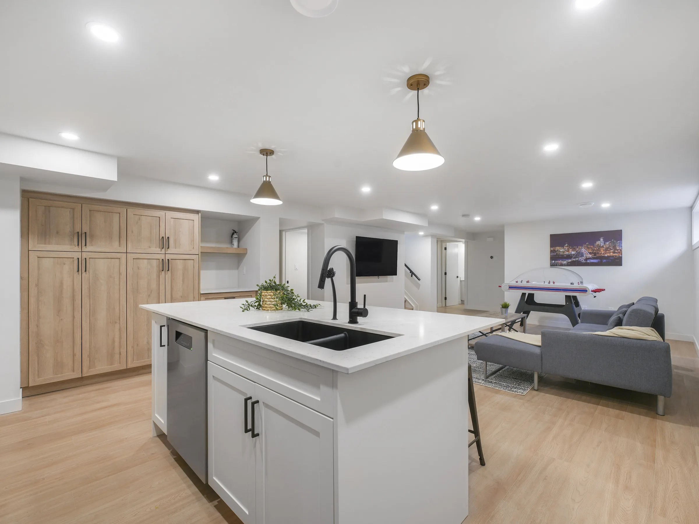 Open kitchen and rec-room layout with tall wood cabinets, TV, stairs and sofa