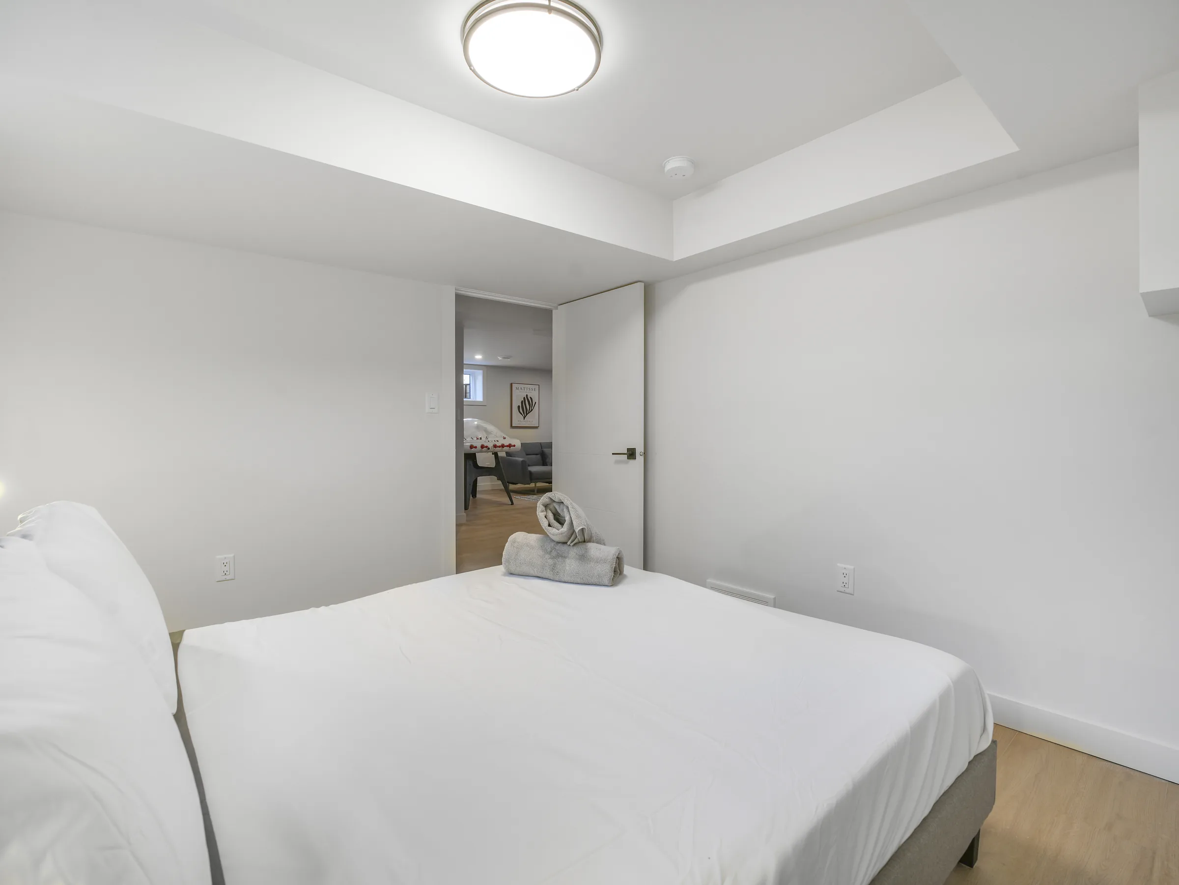 Basement bedroom with the door open to the rec room, rolled towels on the bed
