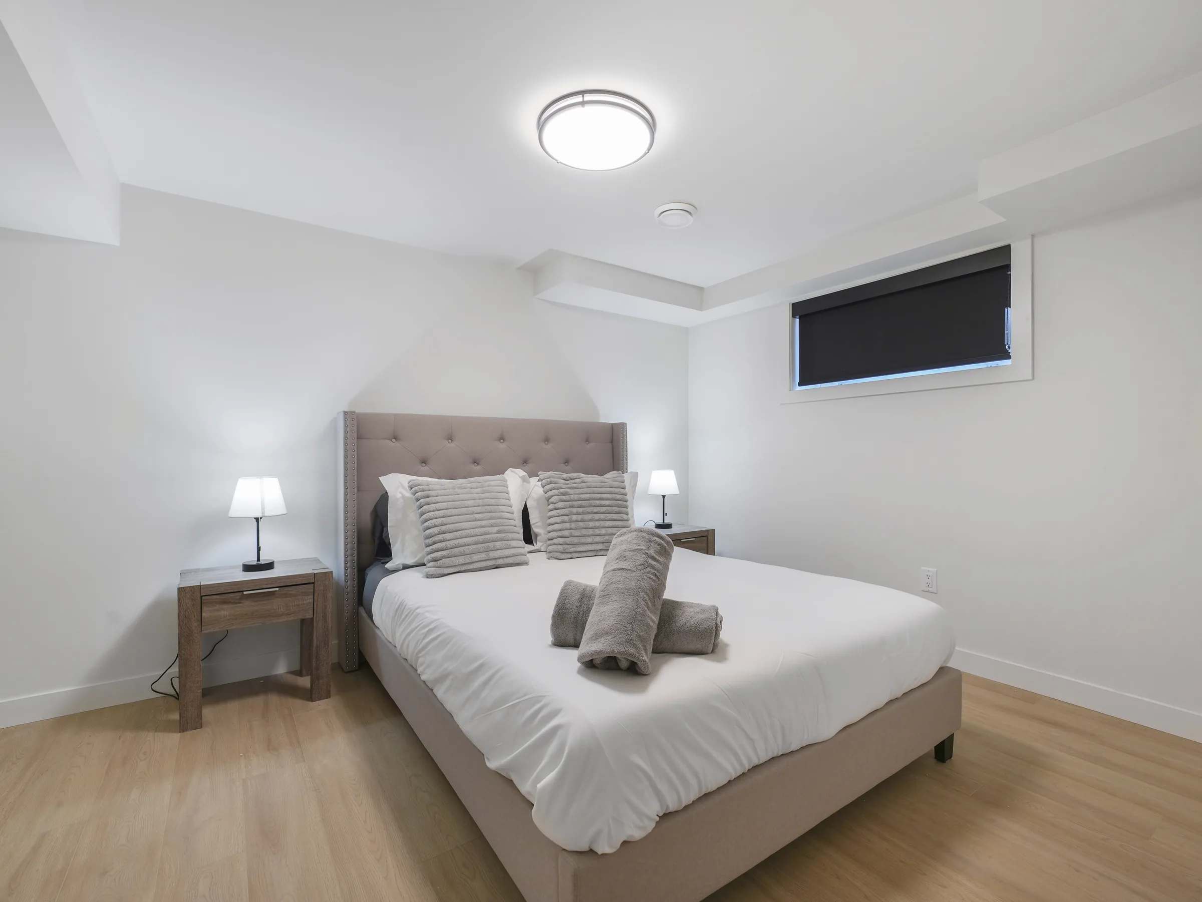 Second basement bedroom with tufted headboard and blackout shade over the window