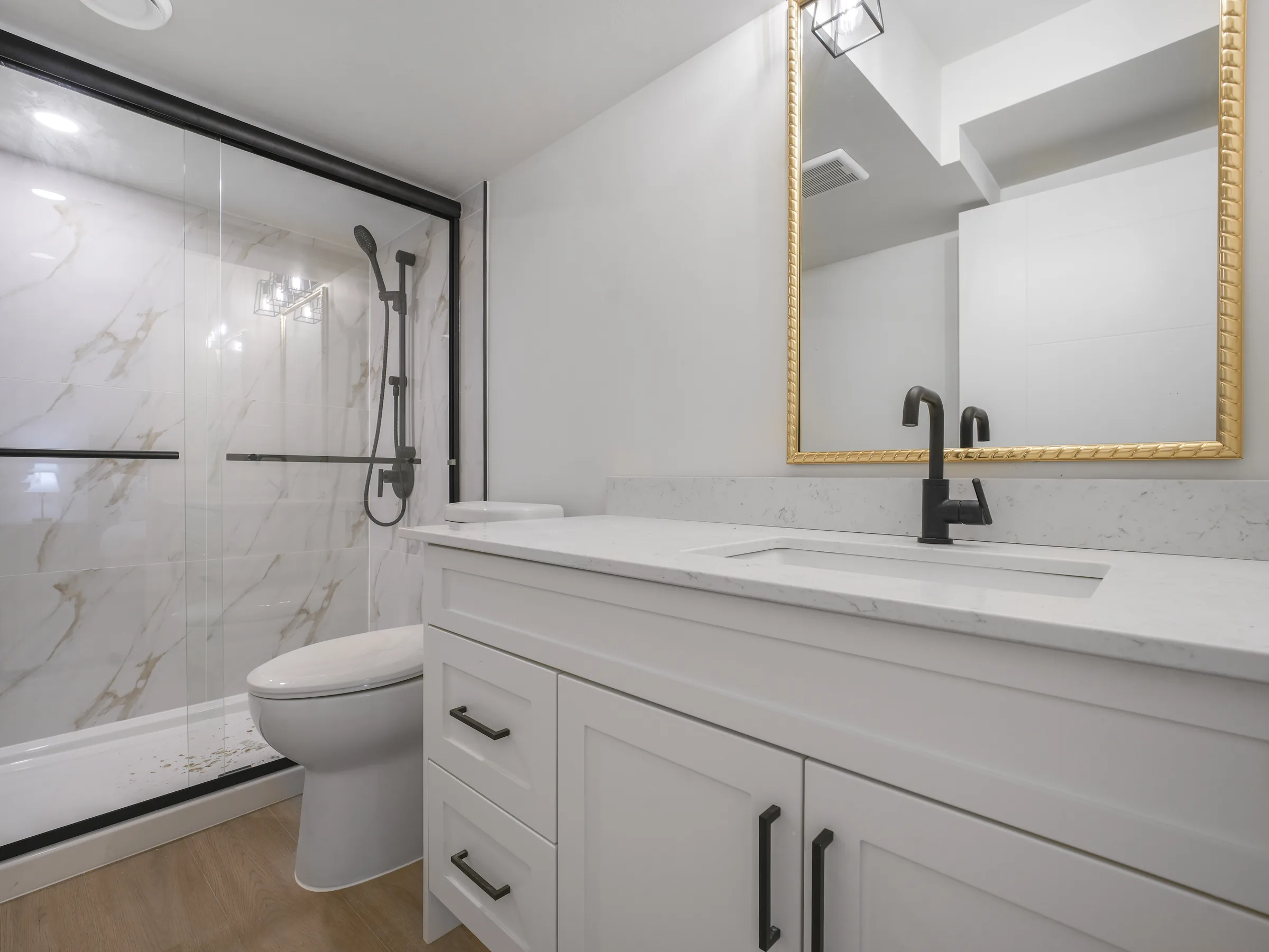 Second bathroom with glass shower and gold-framed mirror
