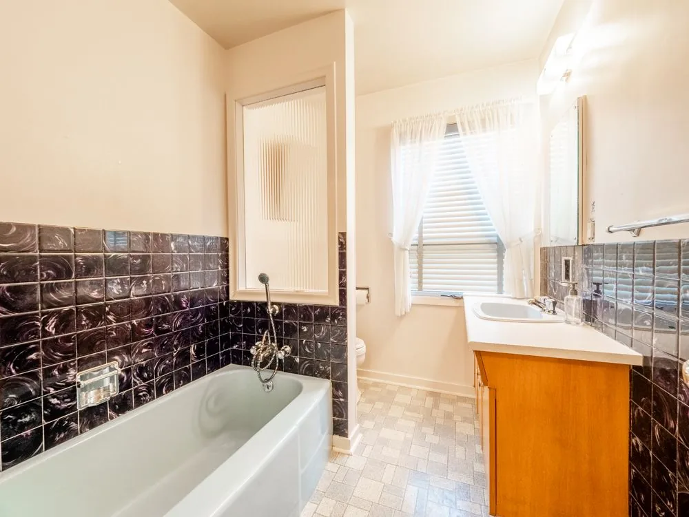 Before renovation, original 1950s bathroom with dark tile tub surround and pedestal-style vanity