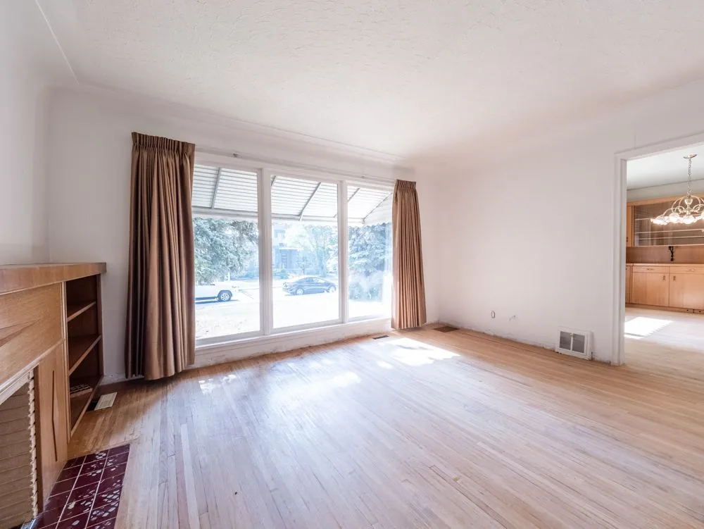 Before renovation, living room with fireplace and large picture window, opens to dining
