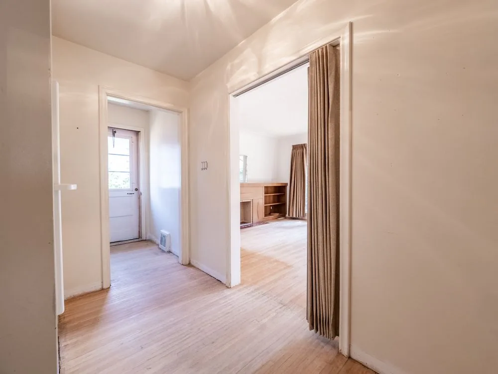Before renovation, back entry hallway with back door and view into the living room fireplace