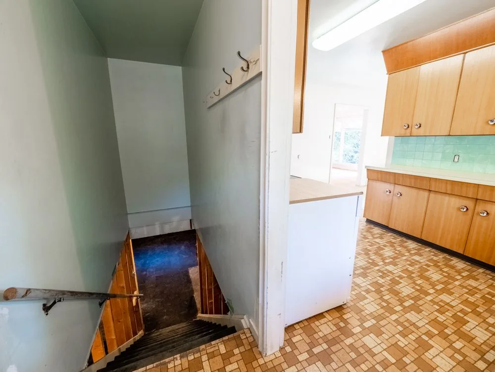 Before renovation, basement stairwell landing off the kitchen with coat hooks