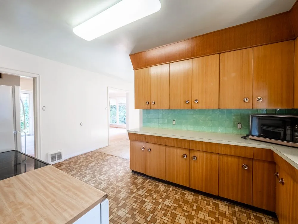 Before renovation, kitchen wide shot with mint tile backsplash, opens to the sunroom/living area