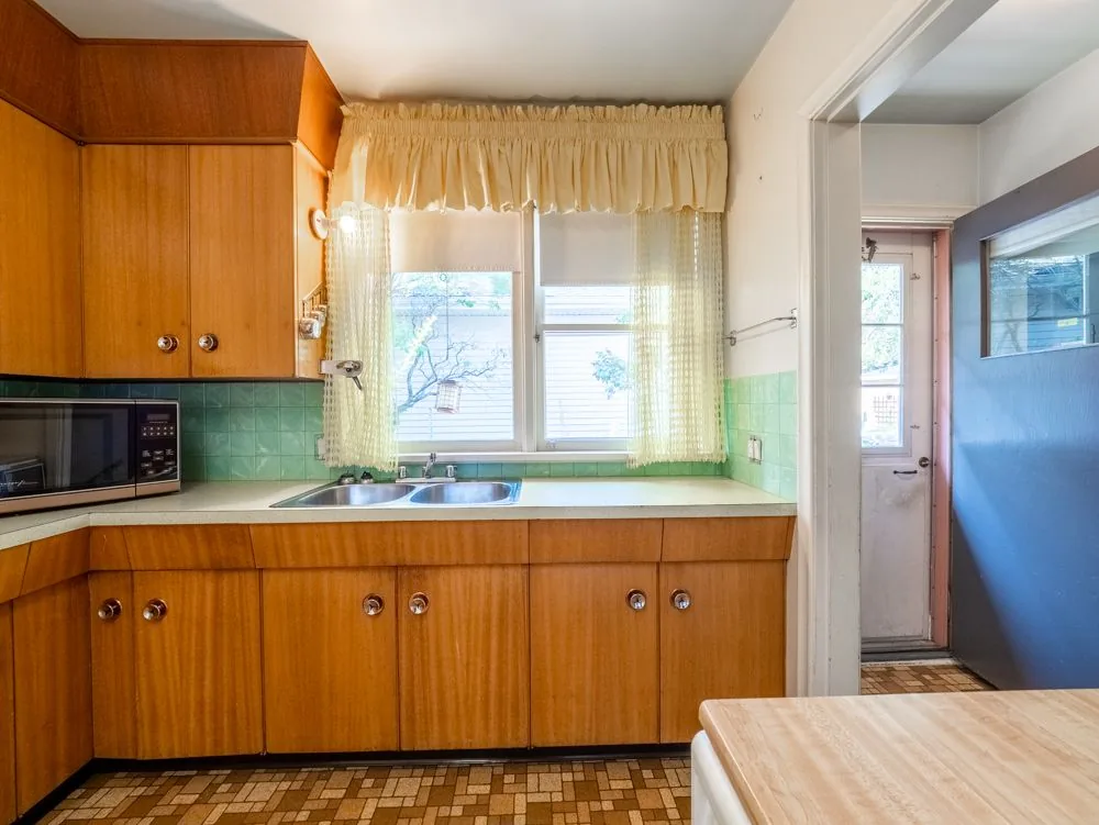 Before renovation, kitchen sink area with yellow curtains, mint tile and back door