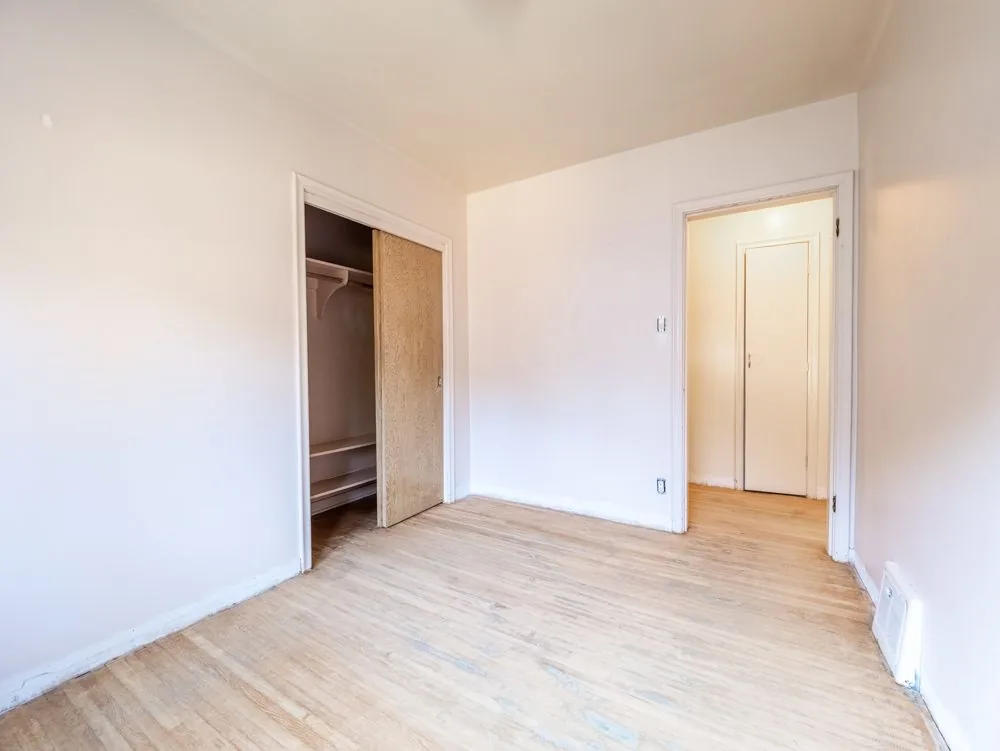 Before renovation, empty bedroom with sliding closet, hallway visible