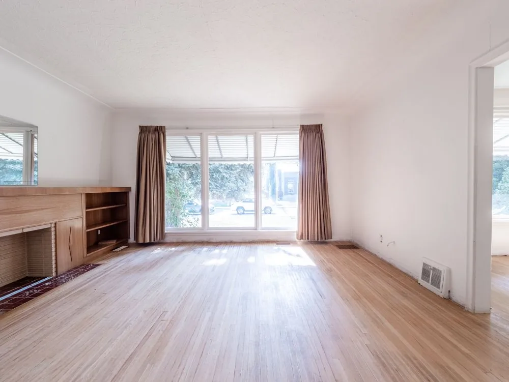 Before renovation, living room with fireplace, mirror and front window overlooking the street