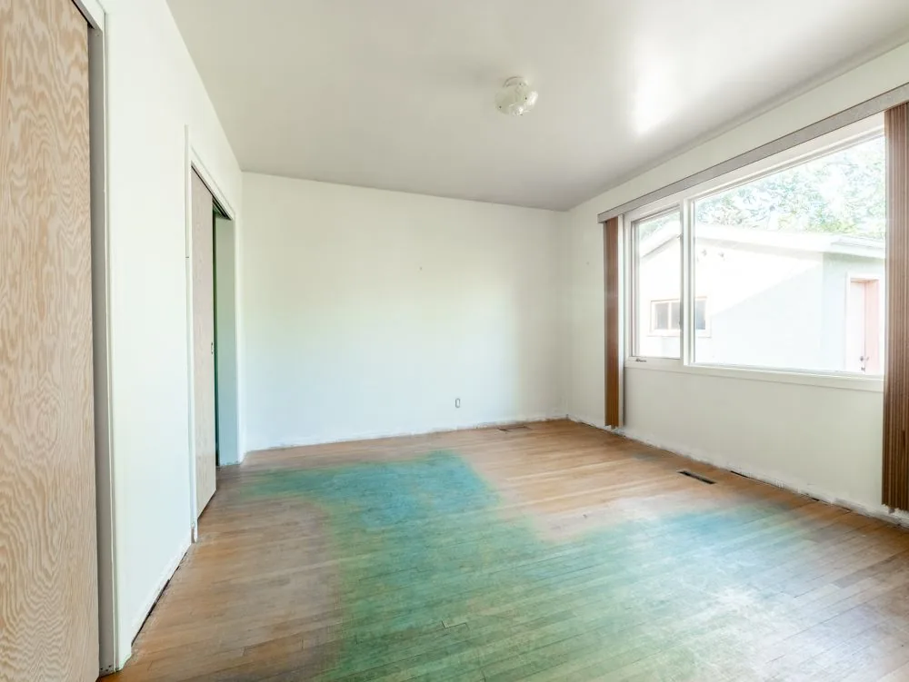 Before renovation, empty bedroom with blue-stained floor patches and side window