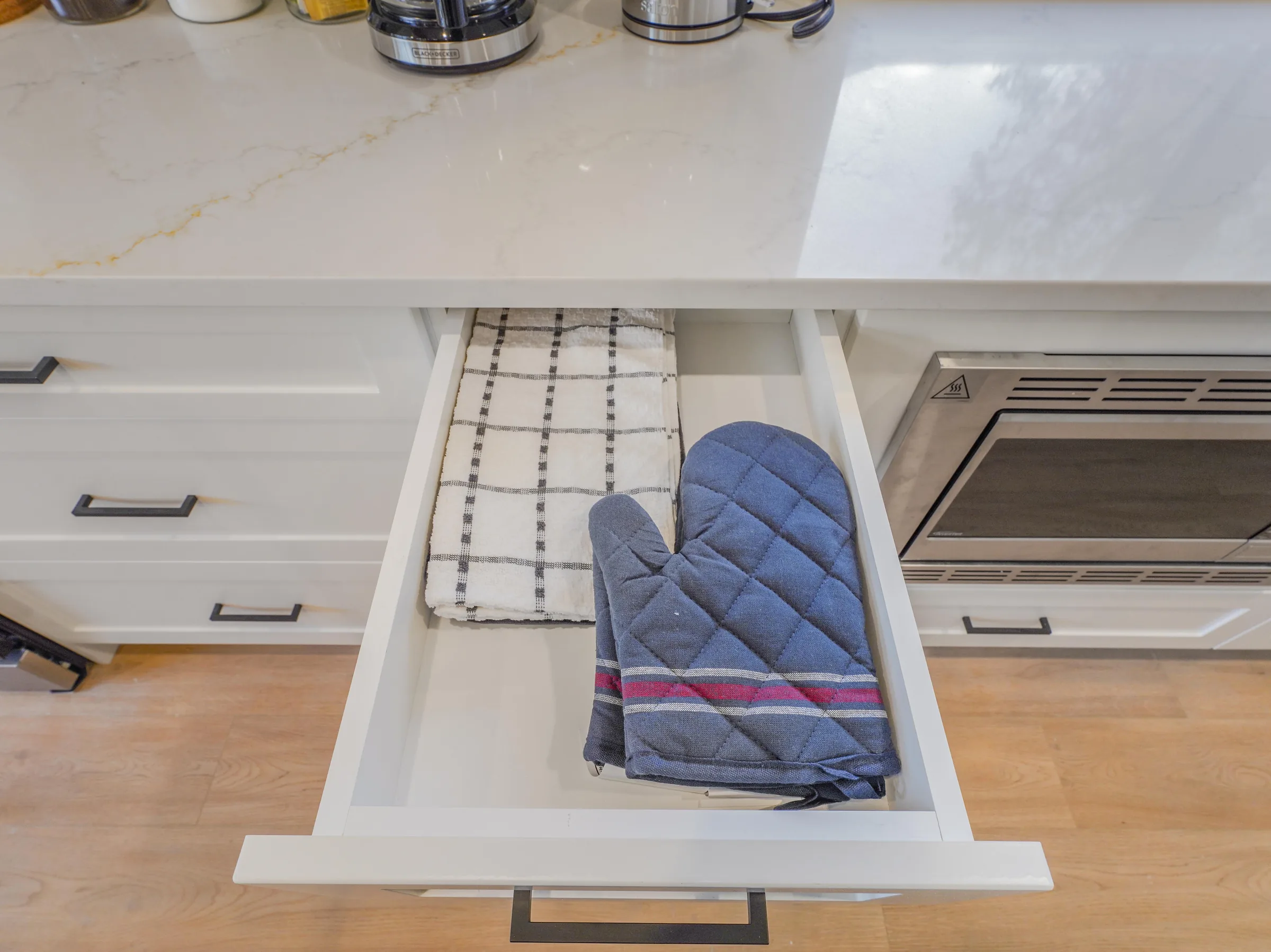 Kitchen drawer open showing oven mitts and towels