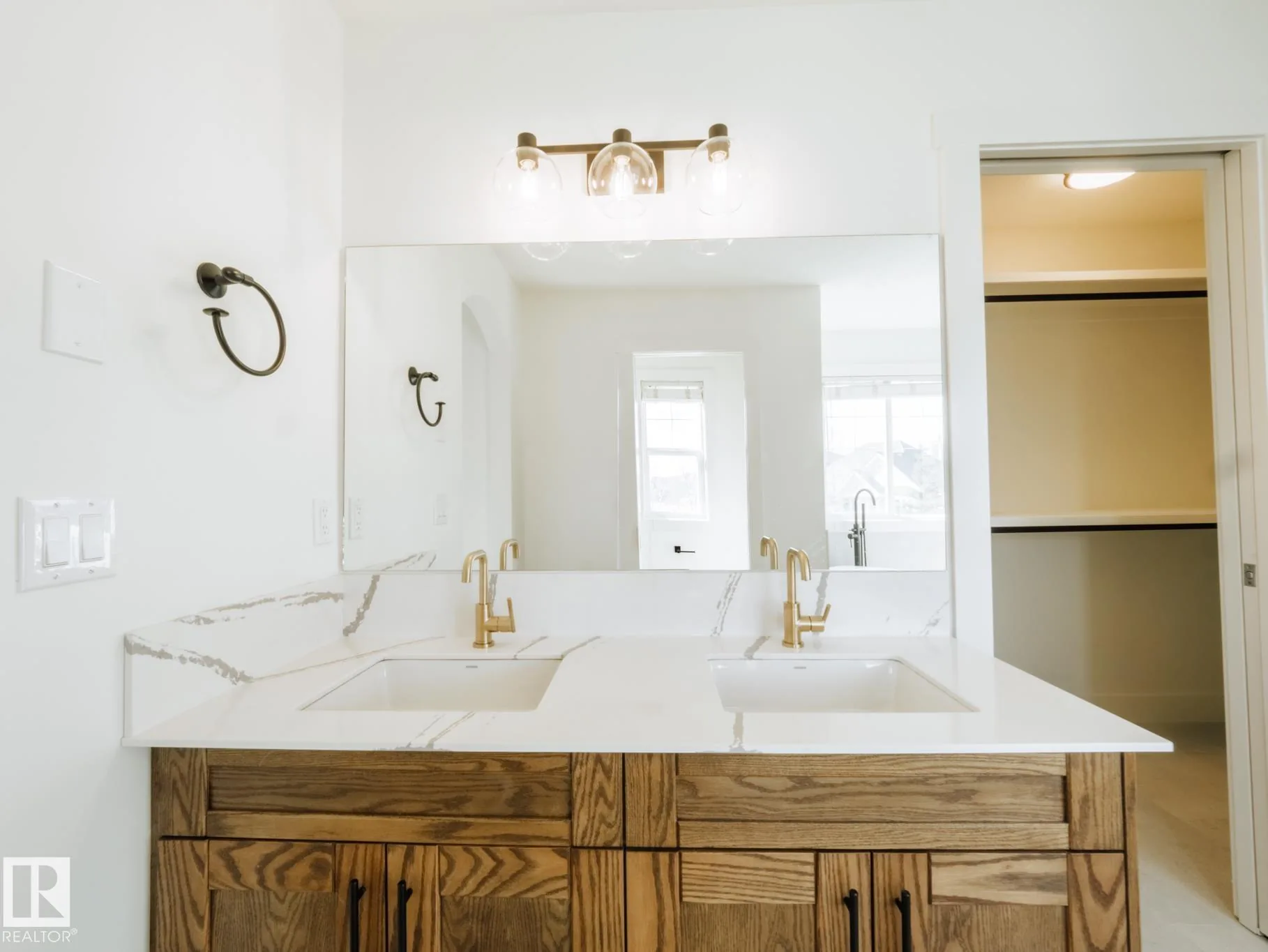 Double vanity with gold fixtures and a view through to the walk-in closet