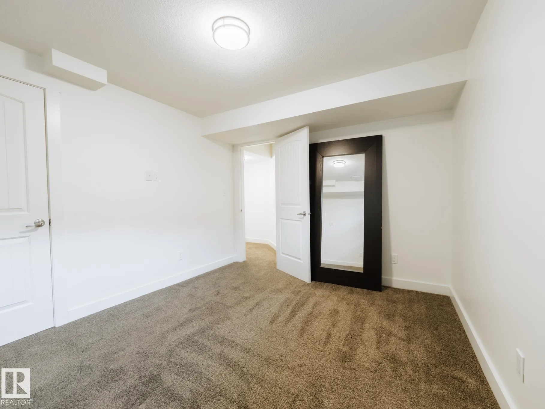 Basement bedroom corner with a dark-framed floor mirror