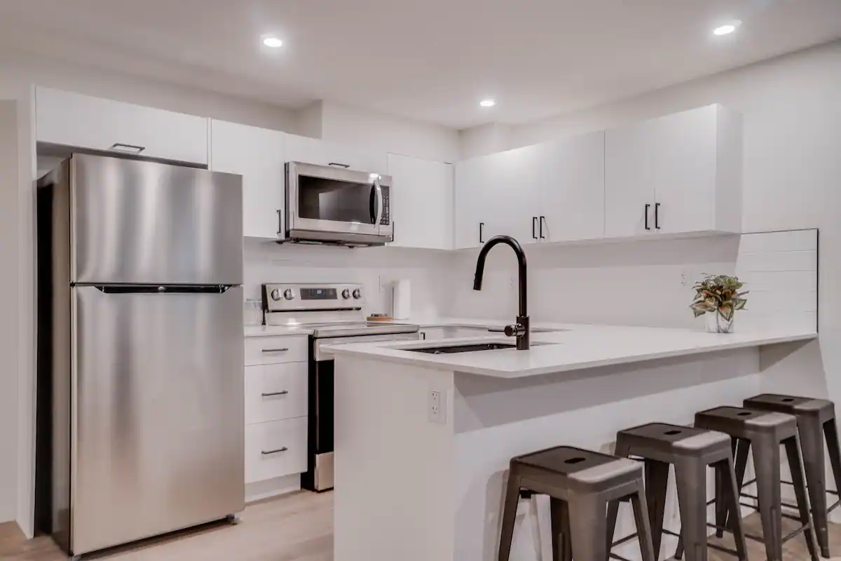 Basement suite kitchen wide view with four counter stools tucked under the white peninsula.