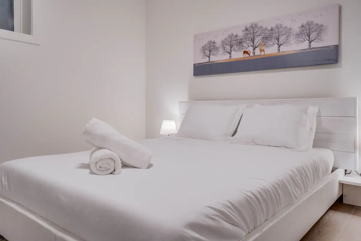 Second basement suite bedroom with white platform bed, white slatted headboard, and a long panoramic canvas of trees and two deer above the bed.