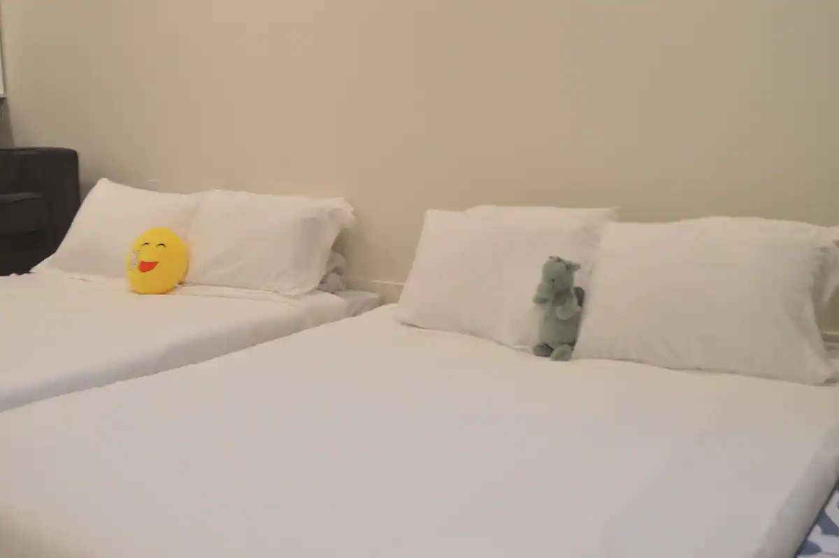 Close-up of the two floor mattresses in the basement suite living room, dressed in white linens with a smiley-face pillow and a stuffed hippo.