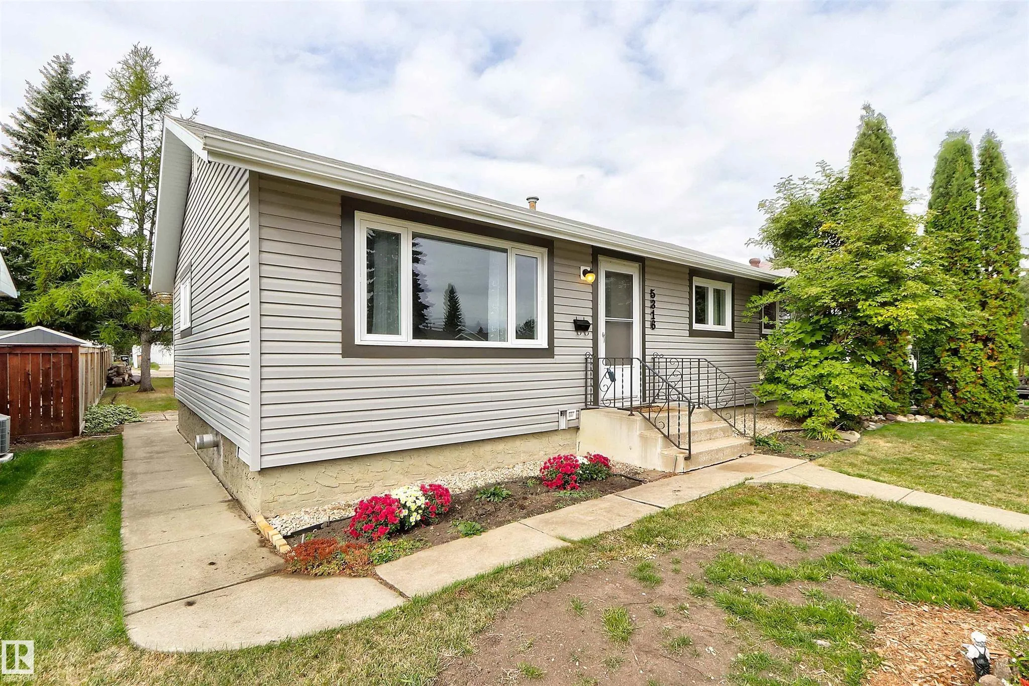 Before renovation, angled front-side view of the bungalow showing the large living-room picture window and side yard.