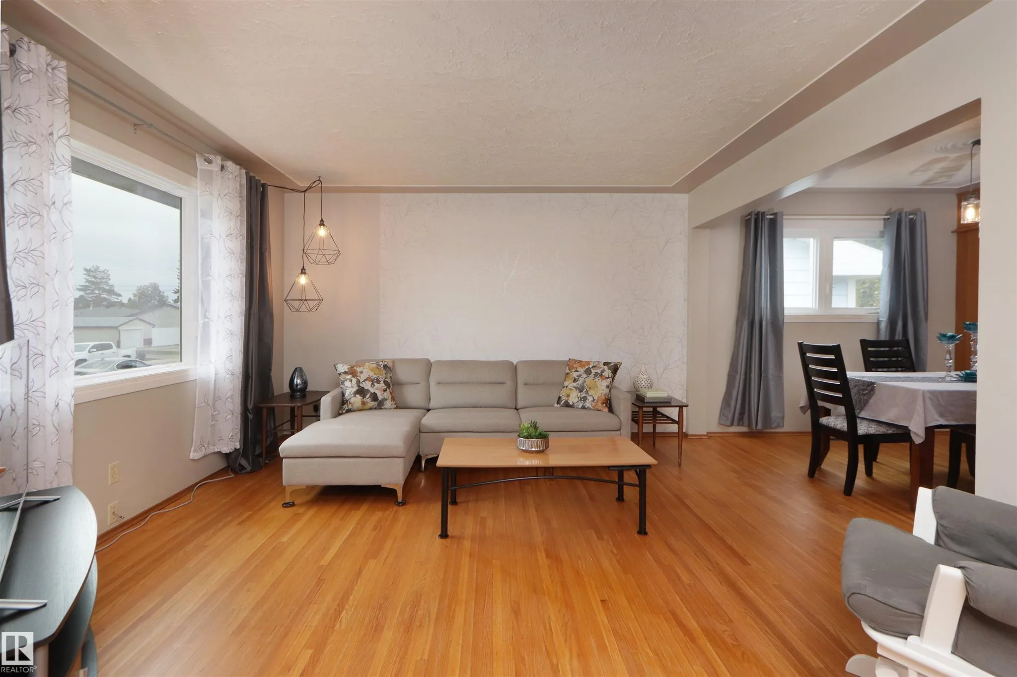 Before renovation, living room from the interior showing the twin front windows and an open view through to the dining area beyond.