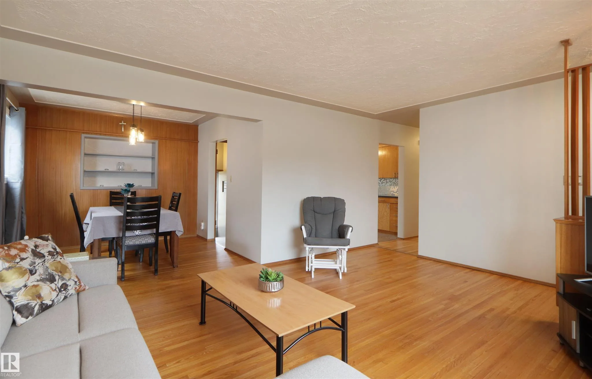 Before renovation, living room angled toward the dining area, showing the dark wood-paneled dining feature wall and a glass-shelf display cabinet.