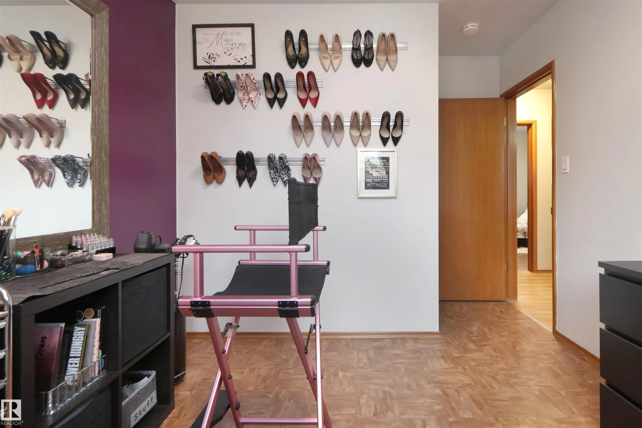 Before renovation, same dressing/makeup room from the opposite angle showing rows of shoes on wire shelves, a pink stool, and the hallway beyond.