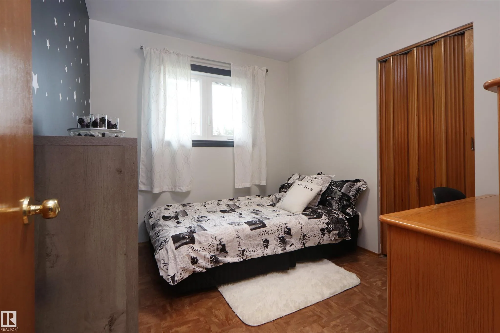 Before renovation, small third bedroom with a star-print accent wall and a twin bed dressed in Paris-print bedding.