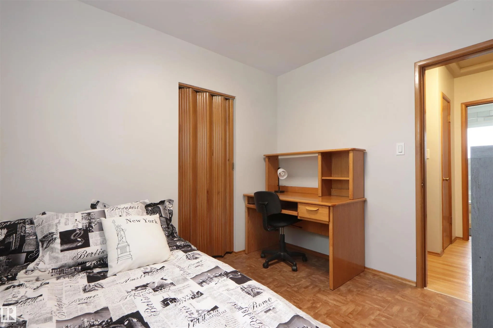 Before renovation, same small third bedroom from another angle showing the wooden hutch desk, twin bed, and view to the hallway.