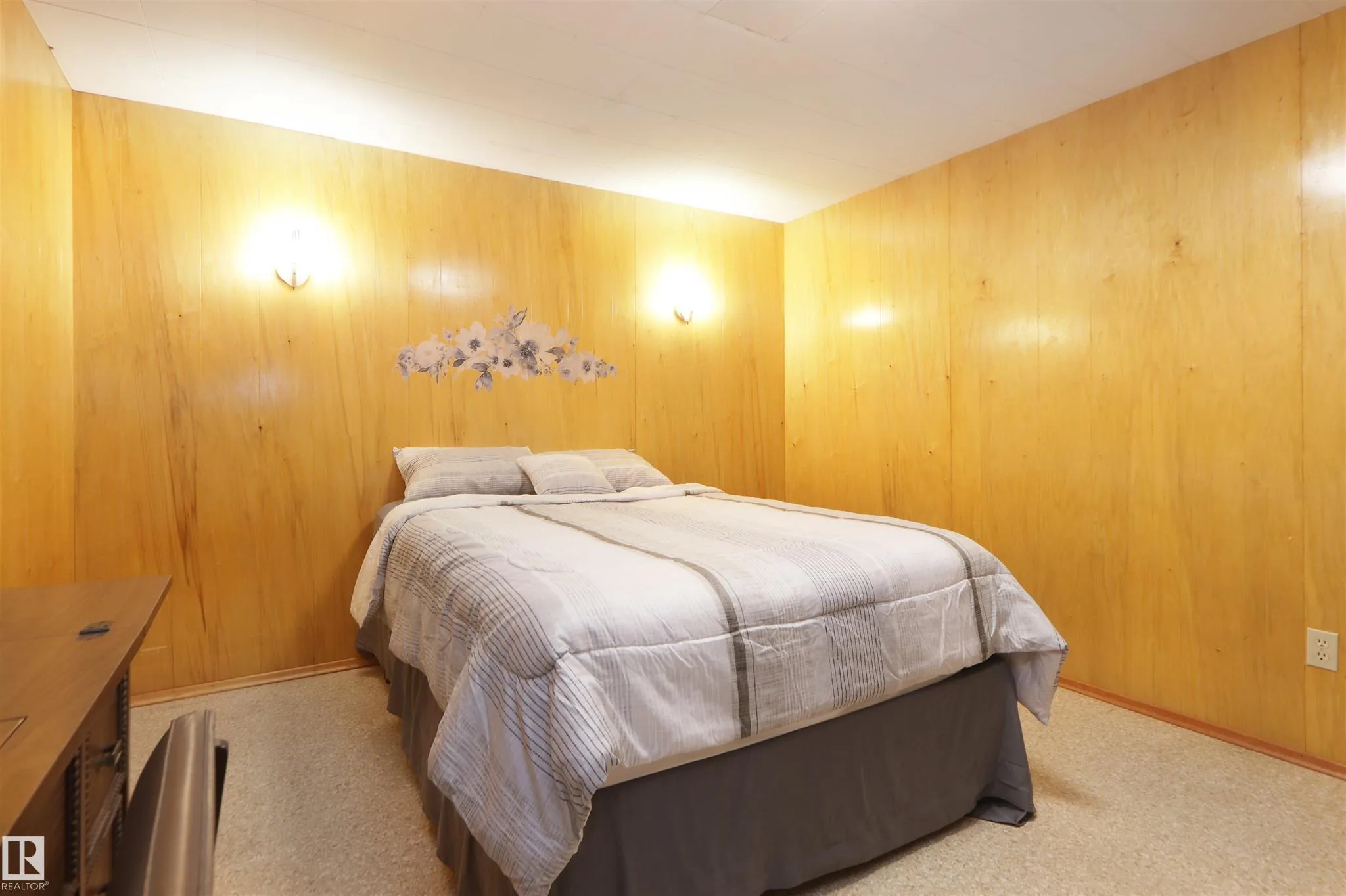 Before renovation, basement bedroom from the foot of the bed showing more of the honey plywood paneling and a small floral wall decal above the headboard.