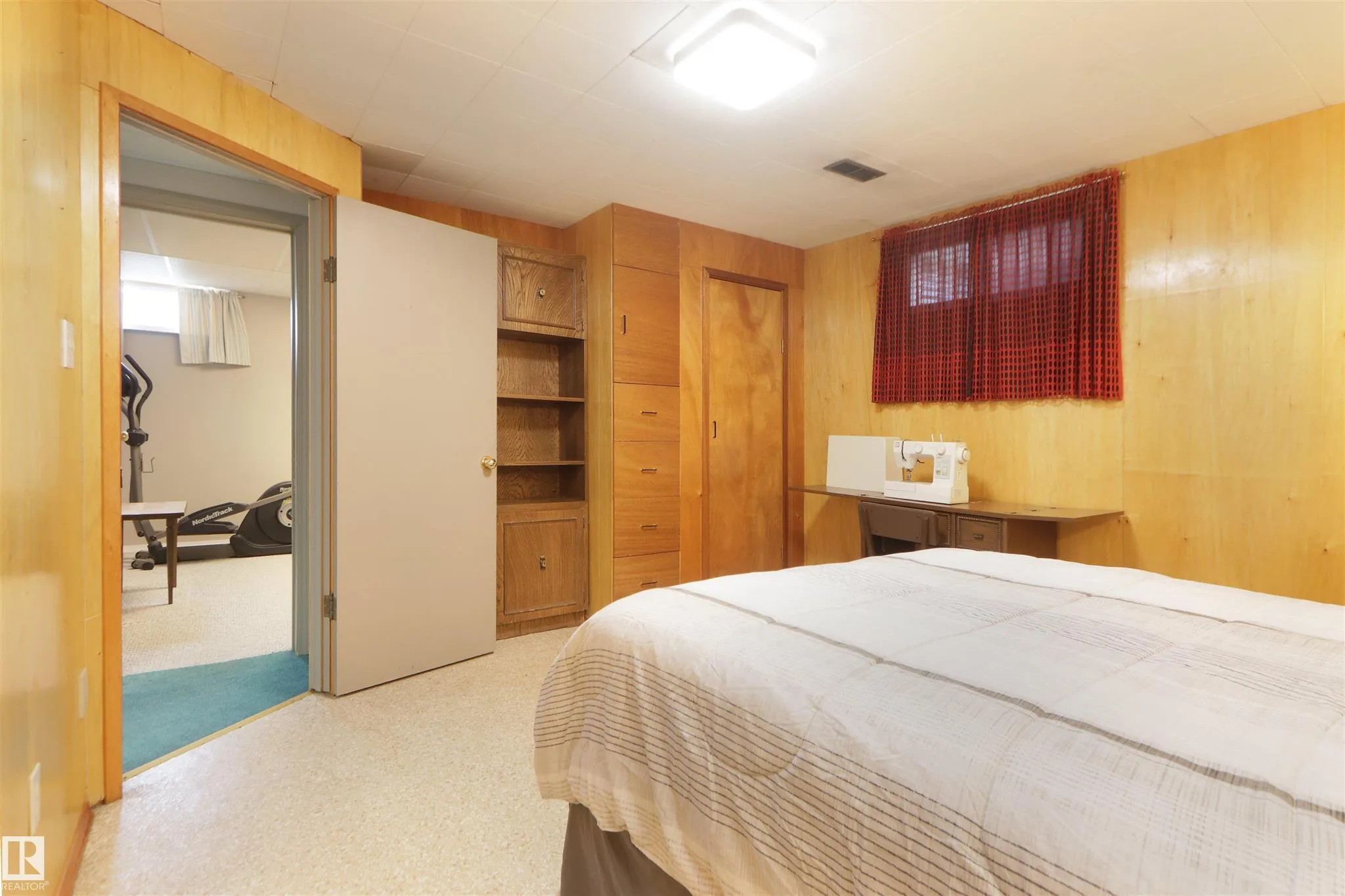 Before renovation, basement bedroom looking toward the open door out to the rec/exercise room, with the built-in oak shelving unit and interior closet door on the near wall.