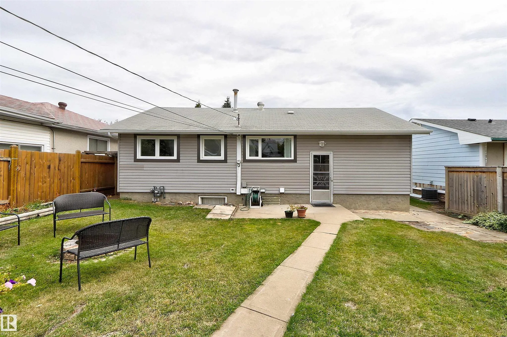 Before renovation, rear elevation of the house with gray horizontal siding, dark trim, and a single storm door up a small concrete stoop.