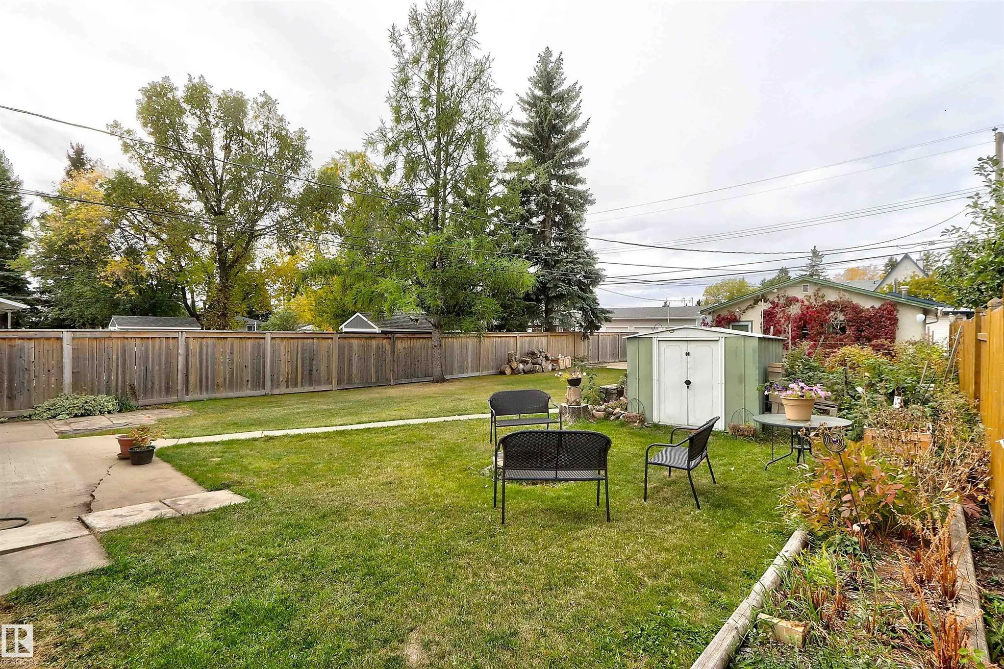 Before renovation, center-yard view showing black iron-frame patio bench and chair, small round metal table, and the tool shed at the back fence.