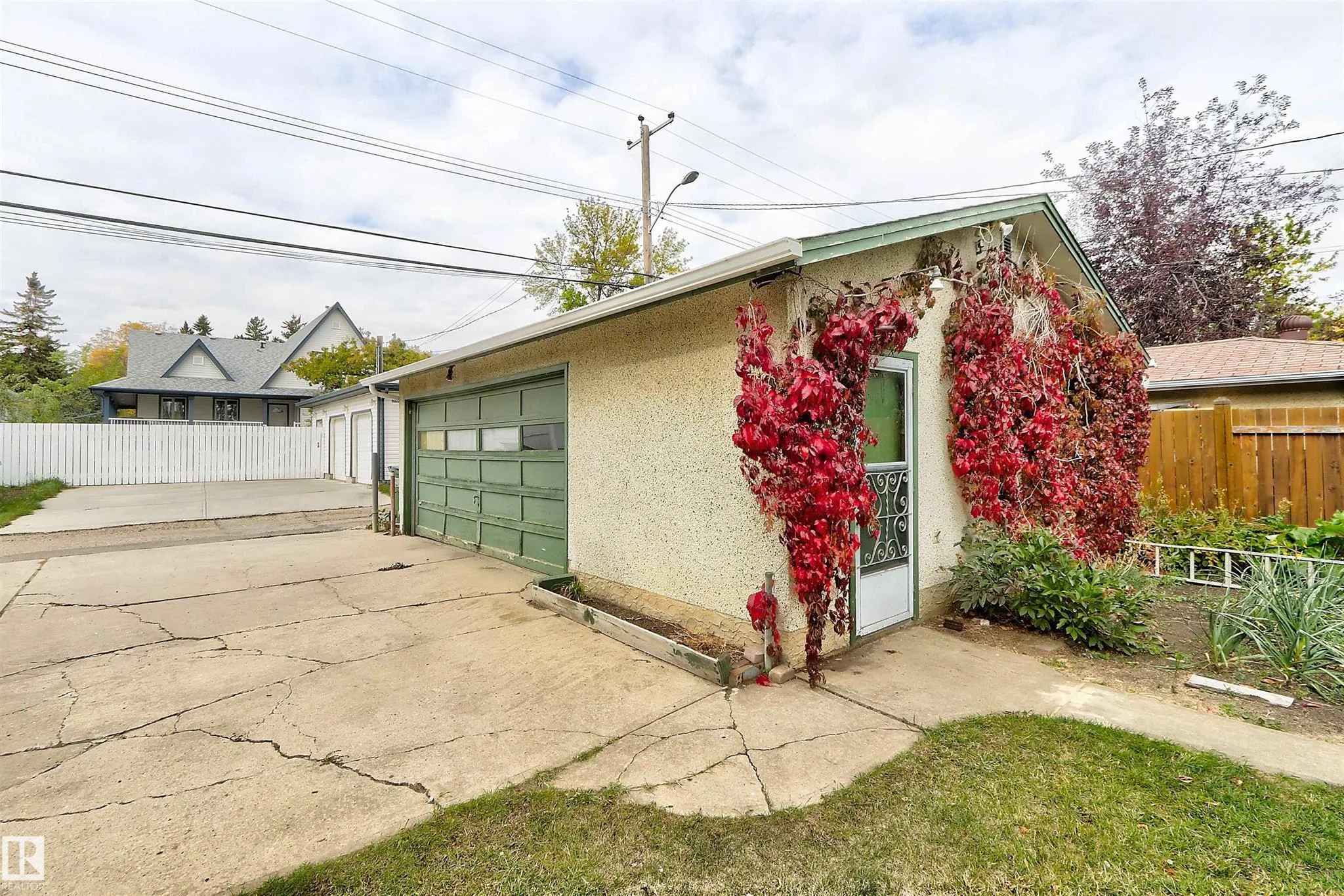 Before renovation, garden-side view of the detached garage showing the man door in the creeper-covered wall and the vegetable garden along the fence.