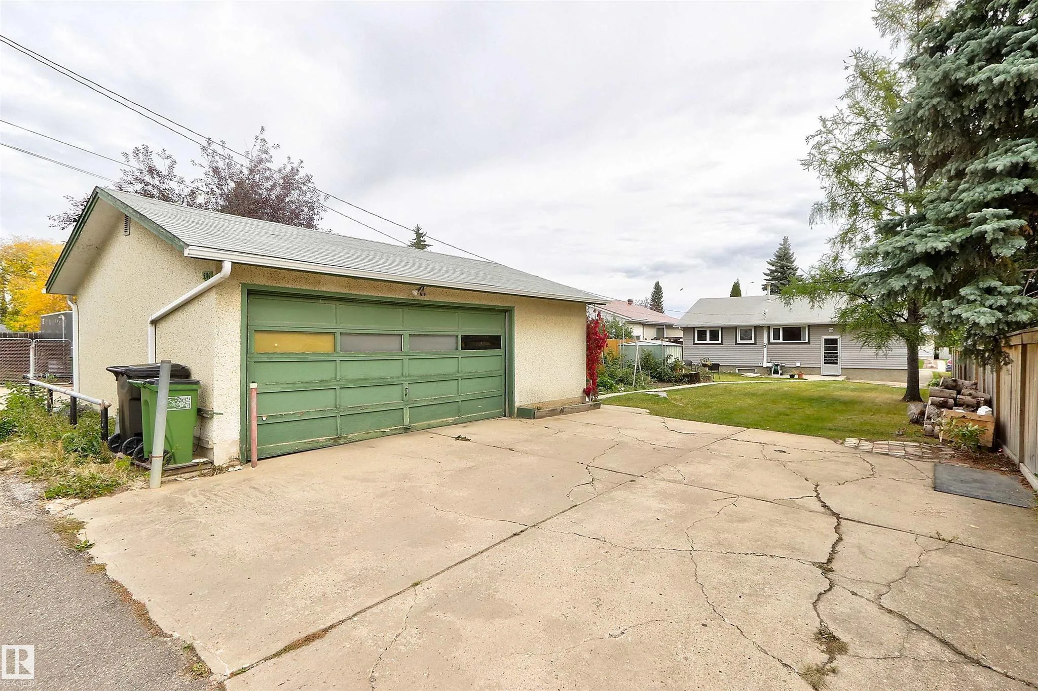 Before renovation, alley-side view of the detached double garage with a green wood-panel double garage door on a cracked concrete pad.