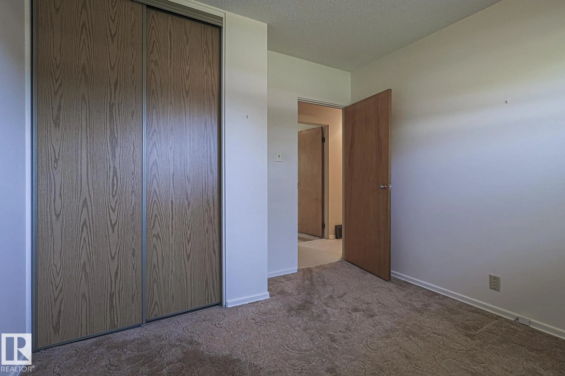 Before renovation, a bedroom with brown patterned carpet, a plywood swing door, and full-width mirrored sliding closet doors.