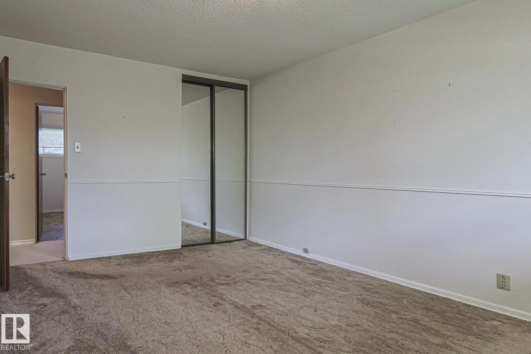 Before renovation, a bedroom with brown patterned carpet, mirrored sliding closet doors, and a plywood door open to the hallway.