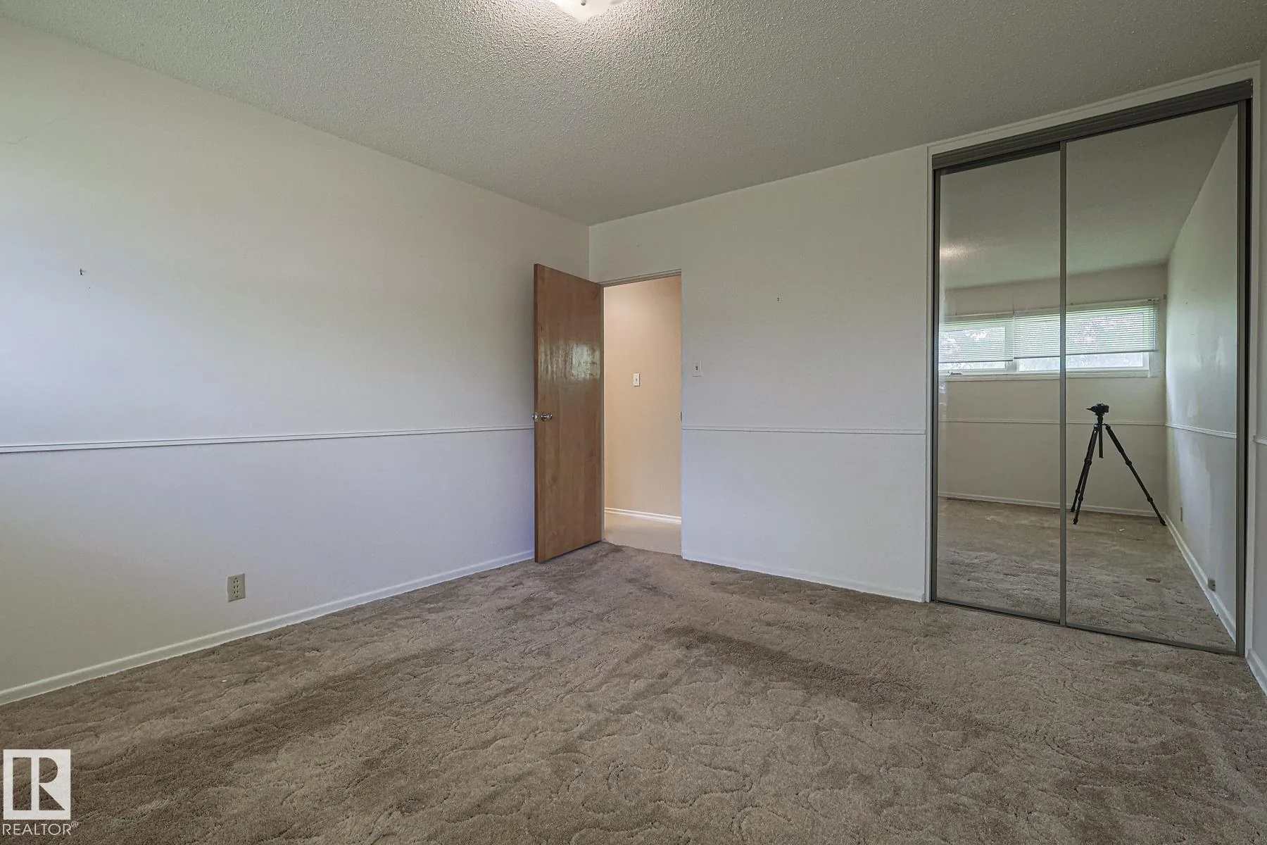 Before renovation, a bedroom with brown patterned carpet, a wood ceiling fan with light kit, and wooden folding louver shutters on the window.