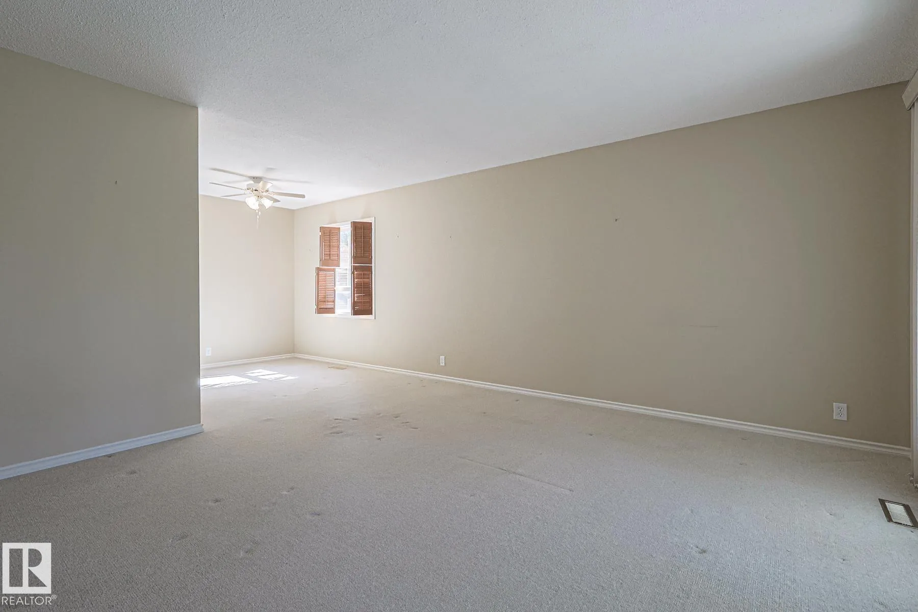 Before renovation, an empty carpeted room with pendant light, plywood door open to a hallway, and light laminate floor visible beyond.
