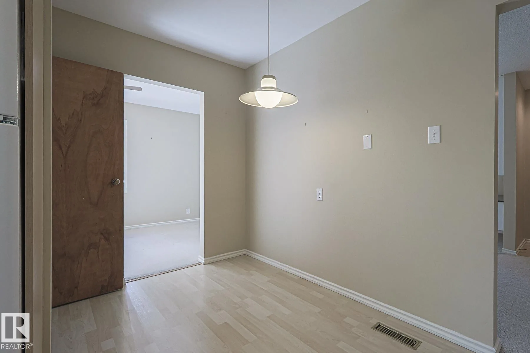 Before renovation, a small dining nook with beige carpet, a modern pendant light, and folding wooden louver shutters on the side window.
