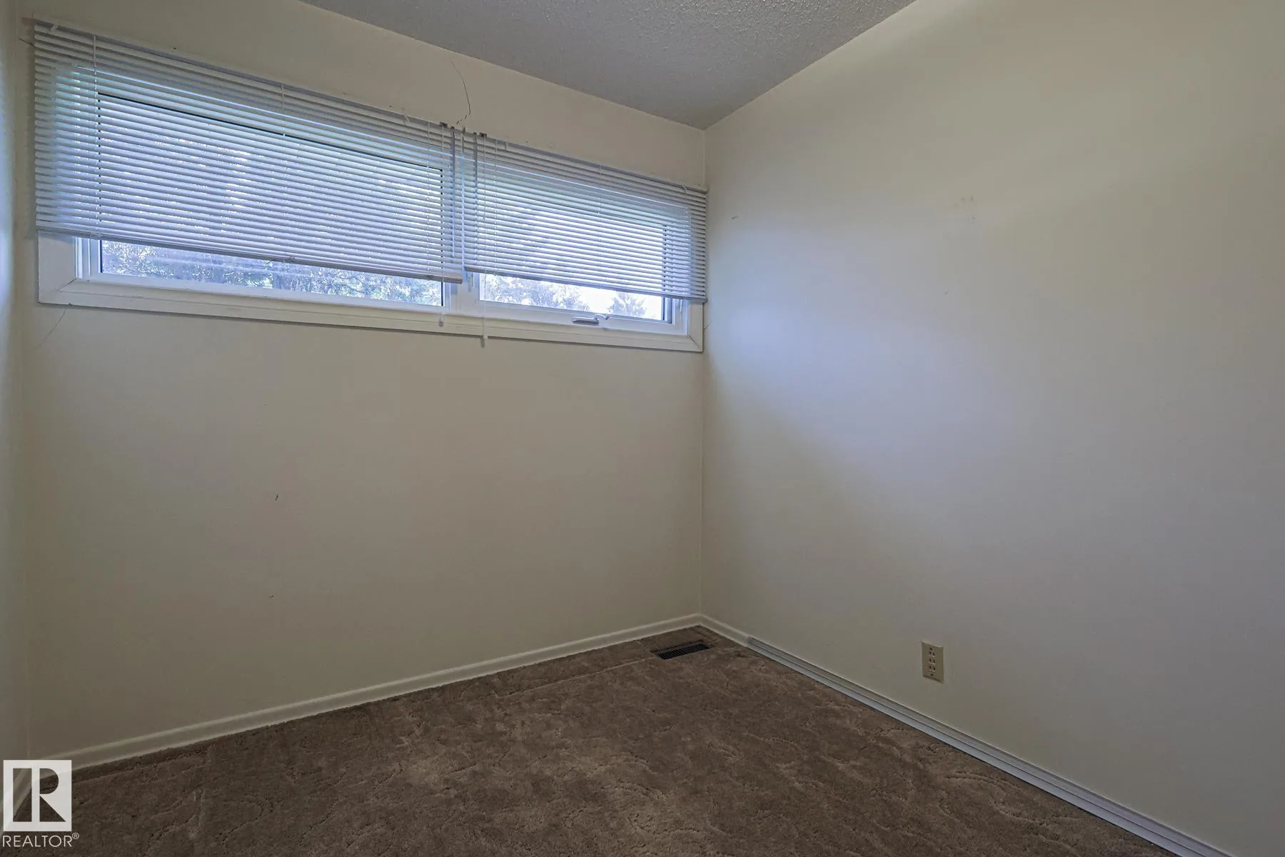 Before renovation, a bathroom with a wall-mounted white pedestal-style sink on chrome legs, a rectangular wall mirror, a toilet with grab-bar frame, and beige carpet on the floor.