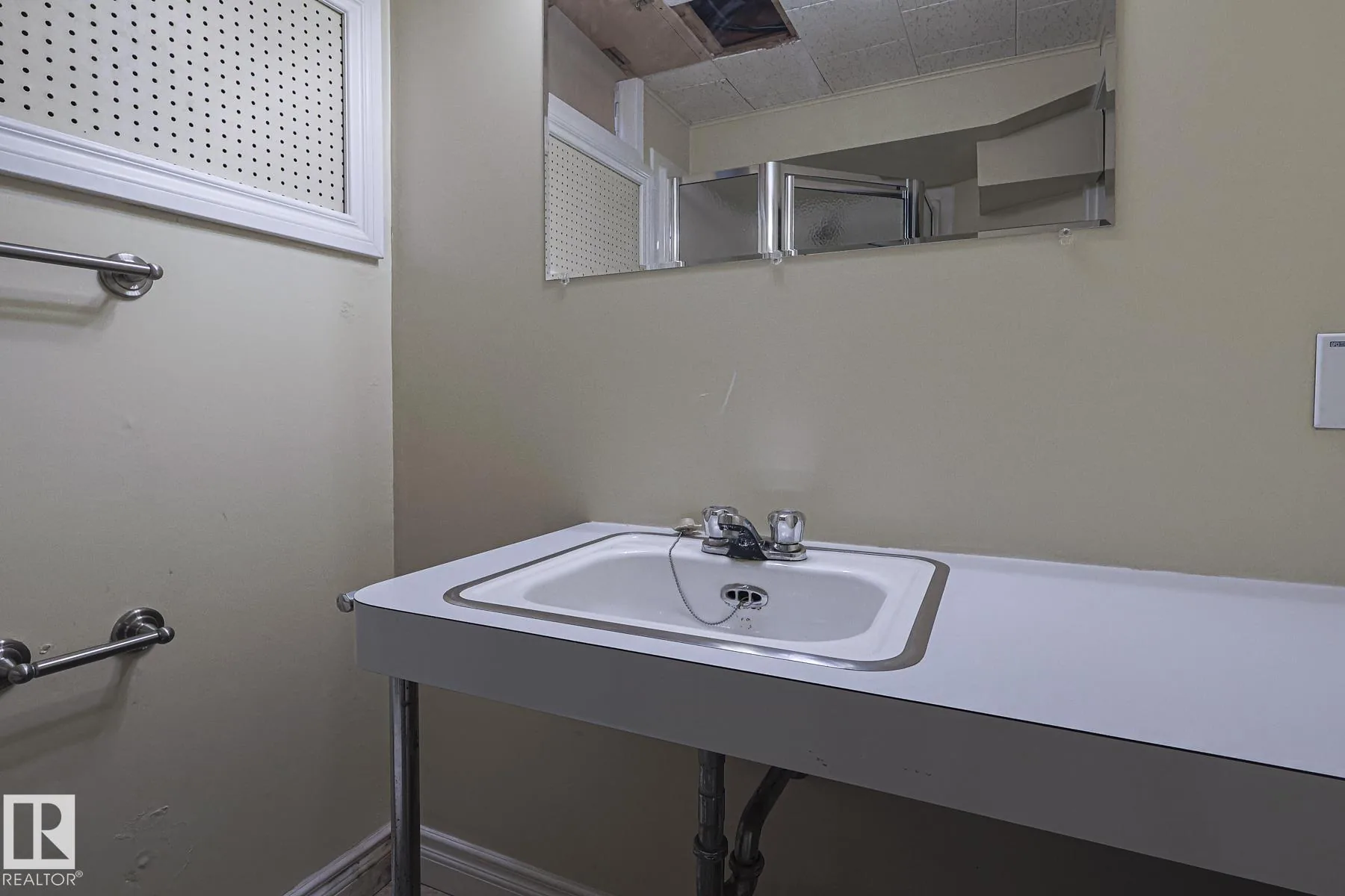 Before renovation, close-up of the basement bathroom's wall-mounted sink with exposed chrome plumbing, chrome twist faucet, and small wall-mounted medicine cabinet.