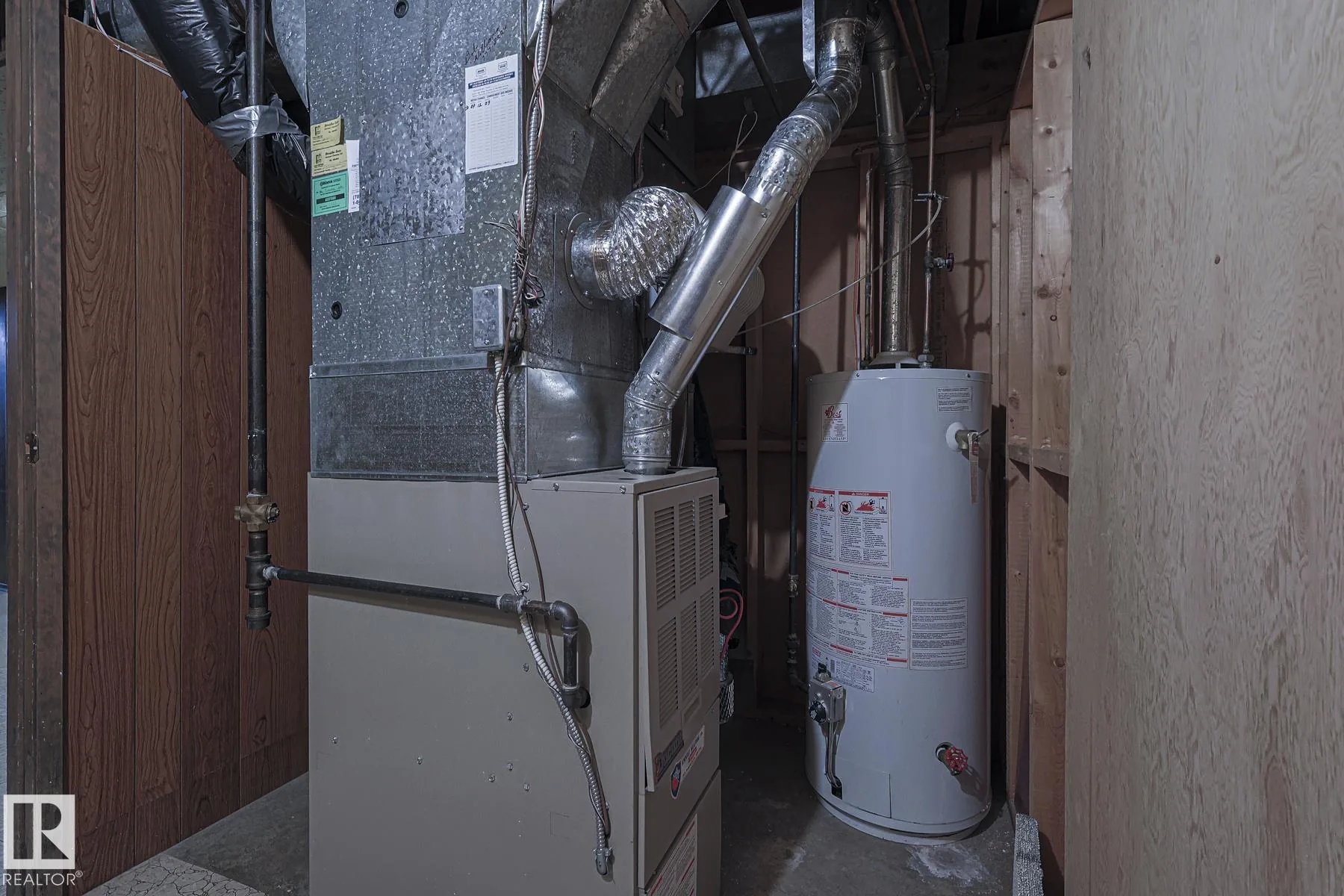 Before renovation, the basement mechanical room with a mid-efficiency forced-air furnace on the left and a gas tank water heater on the right, framed in an unfinished utility closet.
