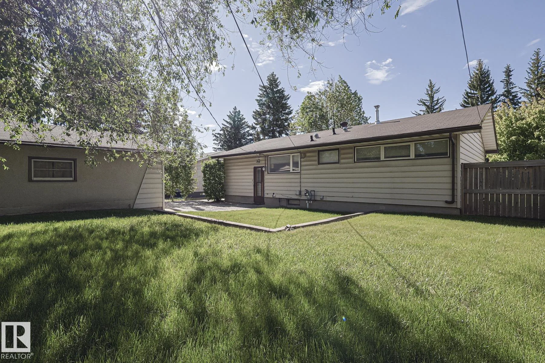 Before renovation, the rear of the house with a small wooden storm door onto the backyard, tan aluminum siding, and a mowed lawn.