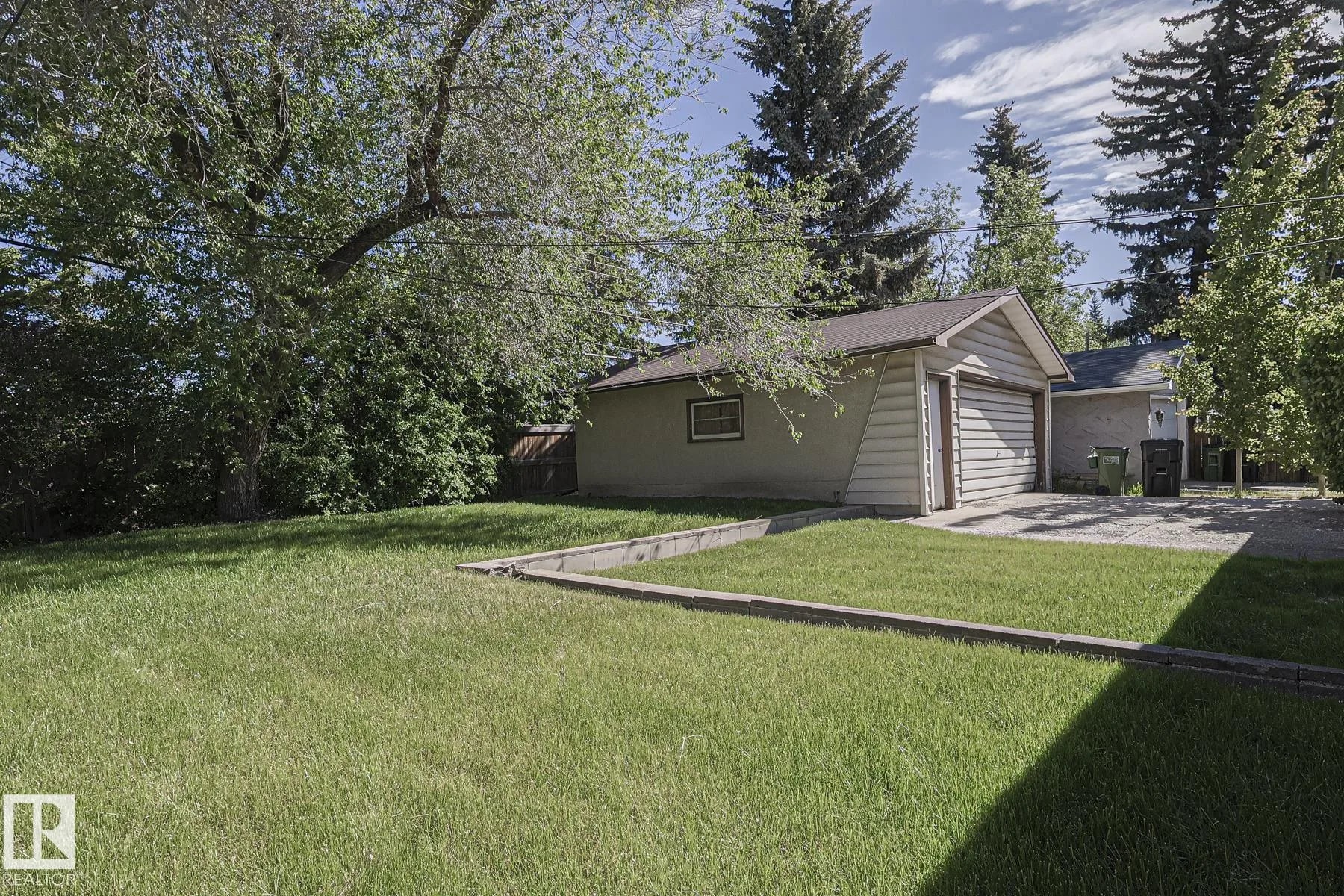 Before renovation, the detached rear garage with cream stucco/siding, a single roll-up door, and a small side window facing the backyard.